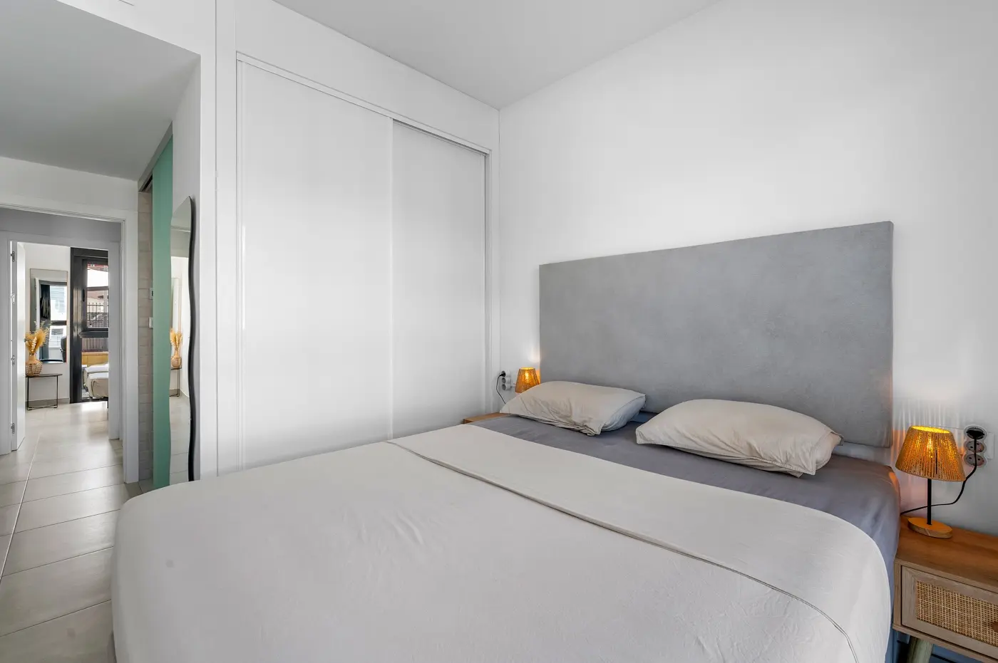 Double bedroom with grey headboard, fitted wardrobes and view down the hallway