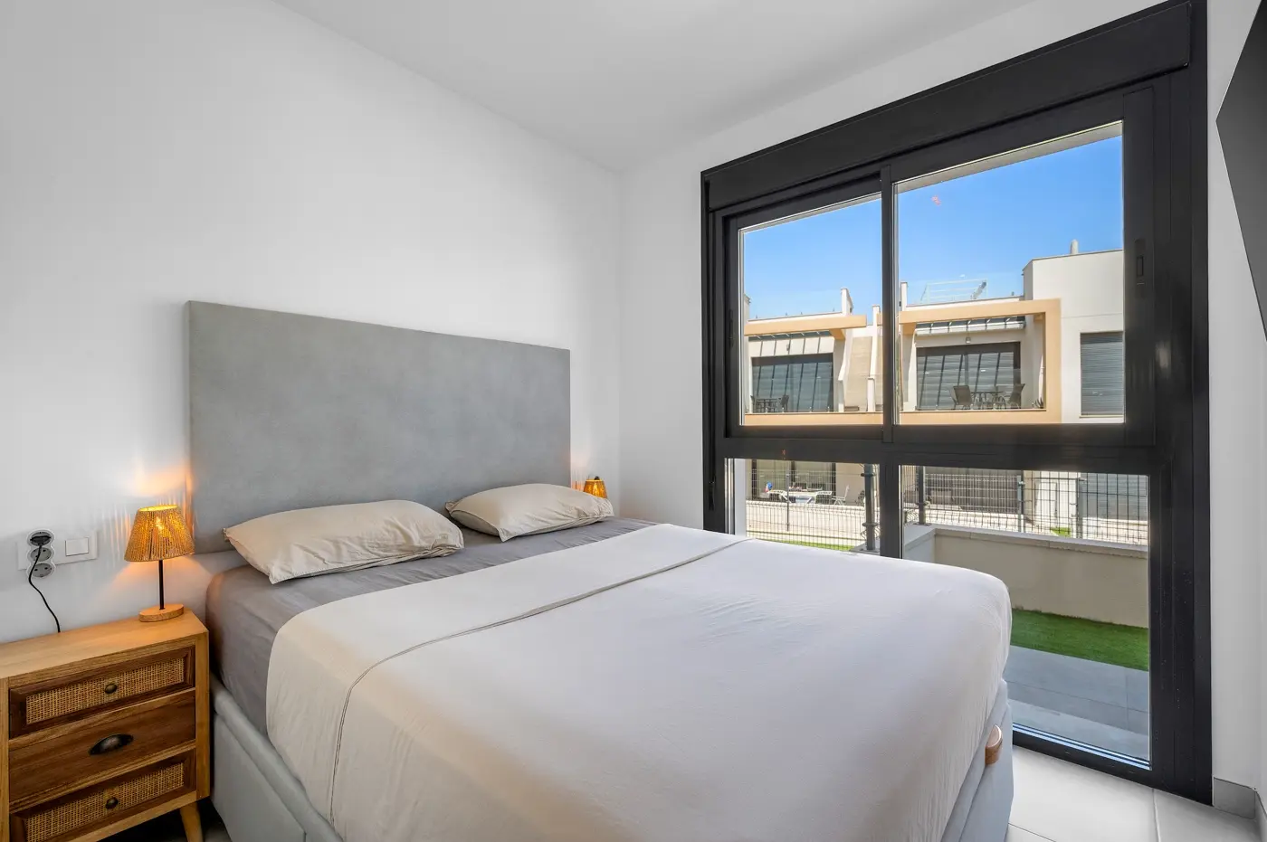 Double bedroom with rattan bedside table and large window onto the terrace
