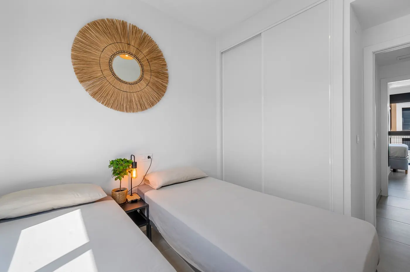 Twin bedroom with woven sun mirror and built-in wardrobe