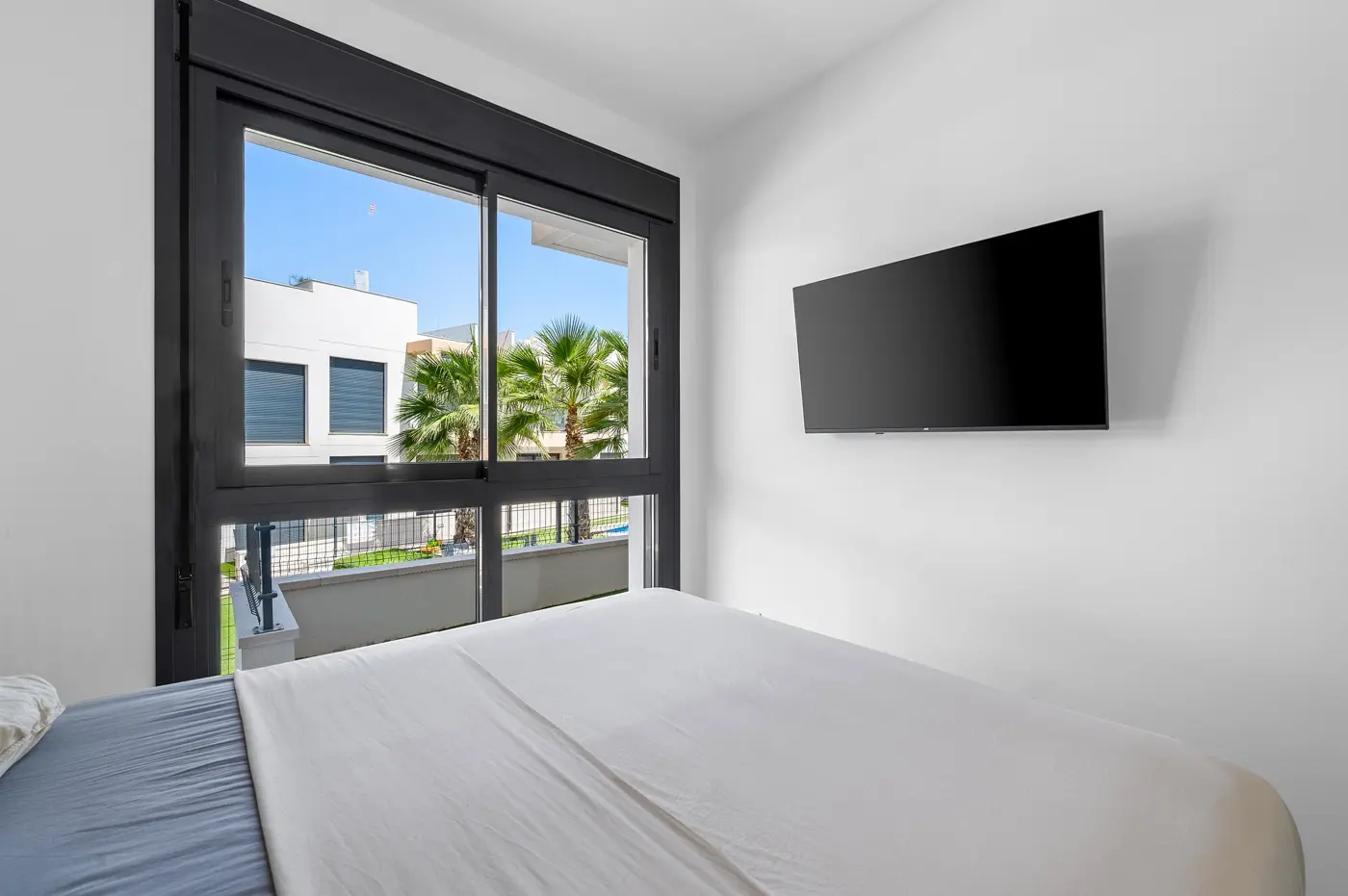 Bright bedroom with wall-mounted TV and palm-tree view through the window