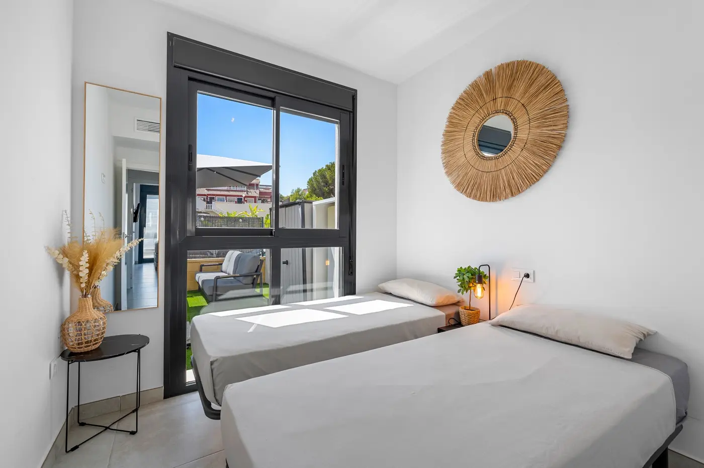 Twin bedroom with woven mirror and sliding door to a private terrace